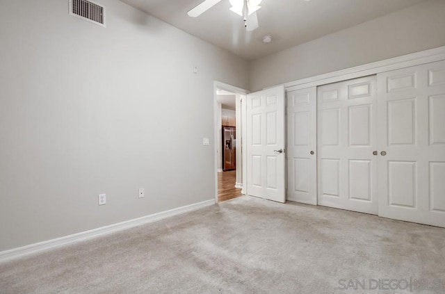 unfurnished bedroom with ceiling fan, a closet, light carpet, and stainless steel fridge with ice dispenser