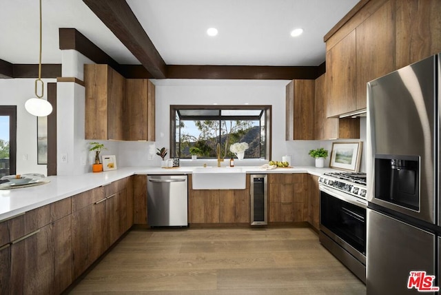 kitchen with appliances with stainless steel finishes, decorative light fixtures, light wood-type flooring, wine cooler, and sink