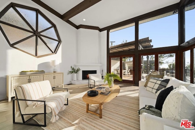 living room featuring a towering ceiling, light hardwood / wood-style flooring, beamed ceiling, and a fireplace