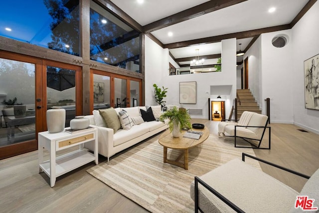 living room with wood-type flooring, a towering ceiling, beamed ceiling, and an inviting chandelier