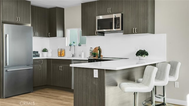 kitchen with appliances with stainless steel finishes, a kitchen breakfast bar, kitchen peninsula, and light hardwood / wood-style floors