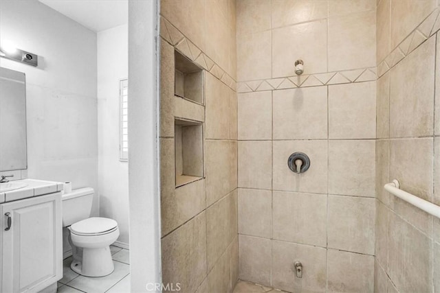 bathroom featuring toilet, tile patterned floors, tiled shower, and vanity