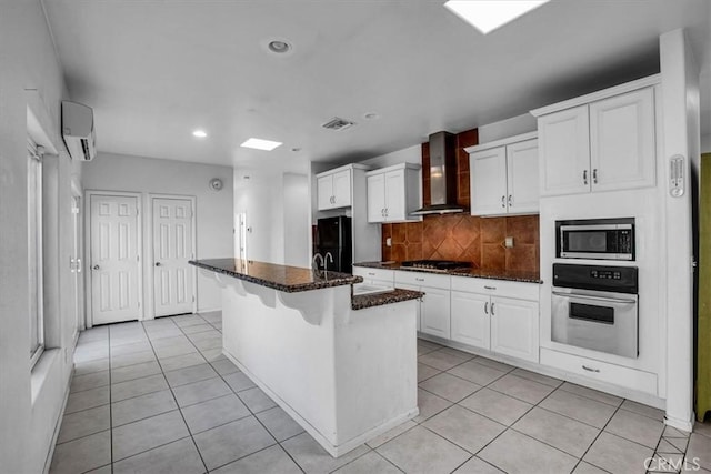 kitchen with appliances with stainless steel finishes, white cabinetry, wall chimney range hood, a center island with sink, and a wall mounted air conditioner