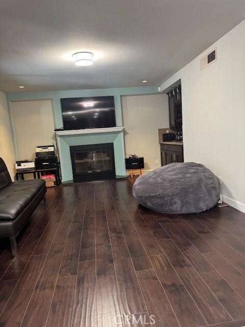 living room with a glass covered fireplace, wood finished floors, visible vents, and baseboards