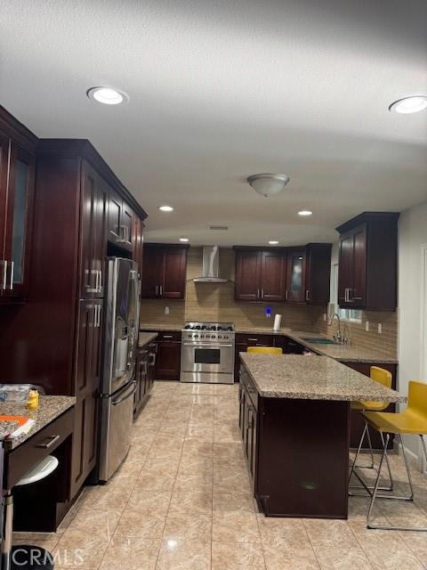 kitchen with a kitchen bar, decorative backsplash, appliances with stainless steel finishes, light stone countertops, and wall chimney exhaust hood