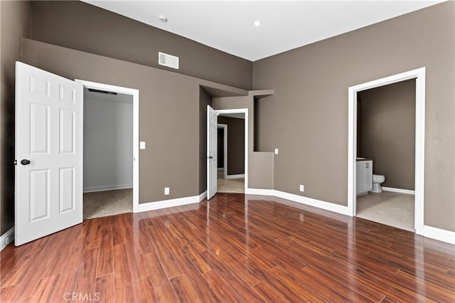 unfurnished bedroom with a closet, ensuite bathroom, and hardwood / wood-style floors