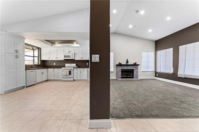 kitchen with a brick fireplace, sink, white appliances, white cabinetry, and light tile patterned floors