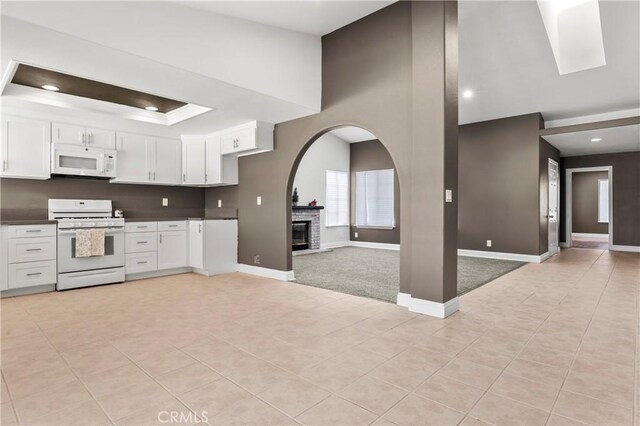 kitchen with light tile patterned floors, white appliances, white cabinets, and a fireplace