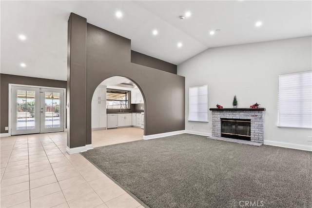 unfurnished living room featuring light tile patterned floors, vaulted ceiling, a fireplace, and french doors