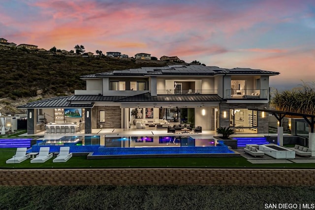 back house at dusk featuring a swimming pool with hot tub, a yard, an outdoor hangout area, a balcony, and a patio