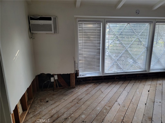 unfurnished room featuring light hardwood / wood-style floors, a wall mounted air conditioner, and beam ceiling