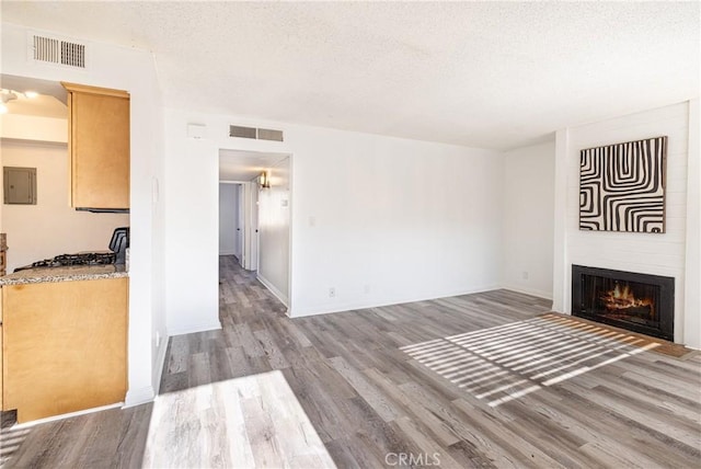 unfurnished living room with a large fireplace, electric panel, a textured ceiling, and hardwood / wood-style floors