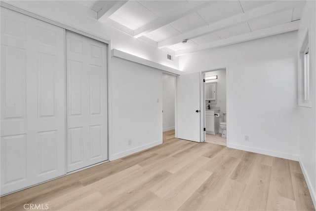 unfurnished bedroom featuring a closet, ensuite bath, beamed ceiling, and light hardwood / wood-style flooring