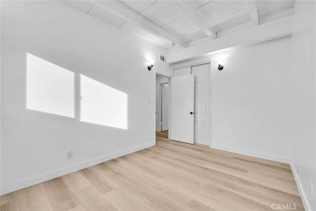 spare room featuring light hardwood / wood-style flooring and beamed ceiling