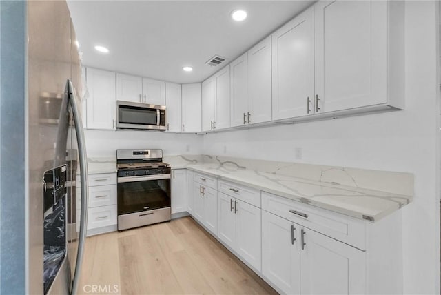 kitchen featuring light hardwood / wood-style floors, light stone countertops, white cabinets, and stainless steel appliances