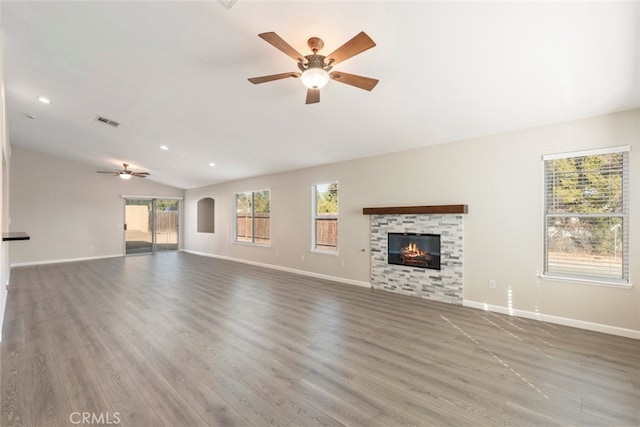 unfurnished living room with ceiling fan, hardwood / wood-style floors, lofted ceiling, and a stone fireplace