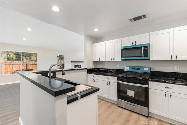 kitchen featuring white cabinets, stainless steel gas stove, sink, light hardwood / wood-style floors, and a center island with sink