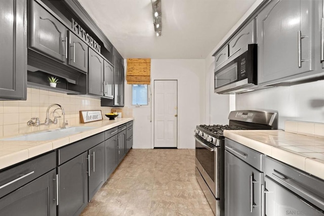 kitchen with backsplash, gray cabinets, sink, appliances with stainless steel finishes, and track lighting