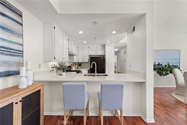 kitchen with white cabinetry, kitchen peninsula, black fridge, range, and sink