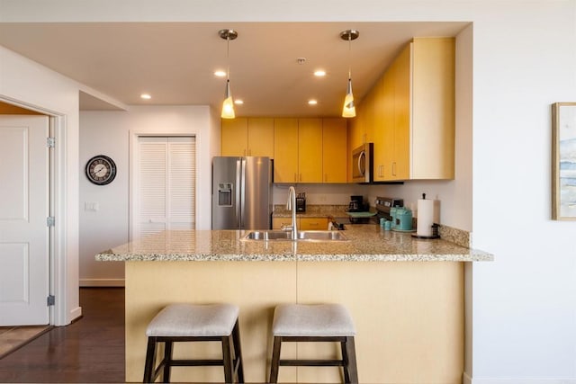 kitchen featuring light stone countertops, pendant lighting, stainless steel appliances, light brown cabinetry, and sink