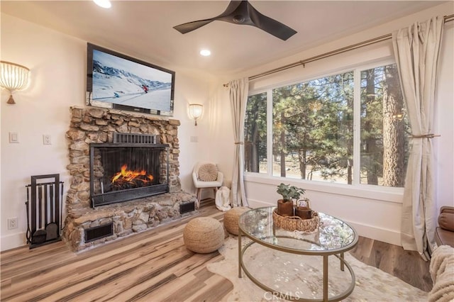 living area featuring ceiling fan, wood-type flooring, and a stone fireplace