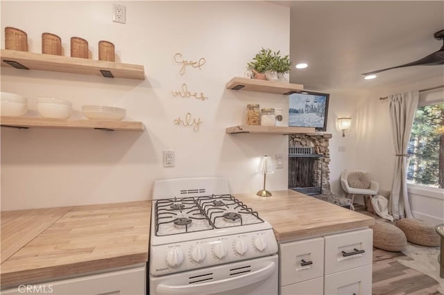 kitchen with a stone fireplace, gas range gas stove, white cabinets, and wooden counters