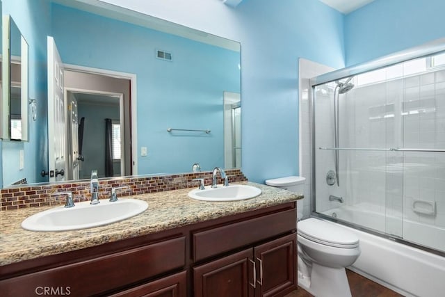 full bathroom with toilet, decorative backsplash, shower / bath combination with glass door, and vanity