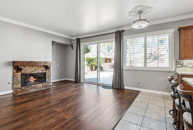 living room featuring light tile patterned floors, crown molding, a stone fireplace, and a healthy amount of sunlight