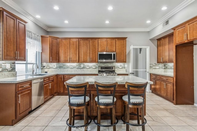 kitchen with appliances with stainless steel finishes, sink, a breakfast bar, ornamental molding, and a kitchen island