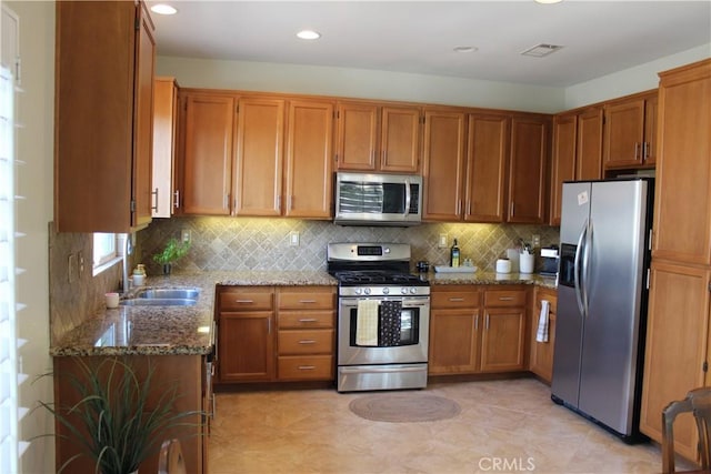 kitchen with appliances with stainless steel finishes, stone countertops, backsplash, and sink