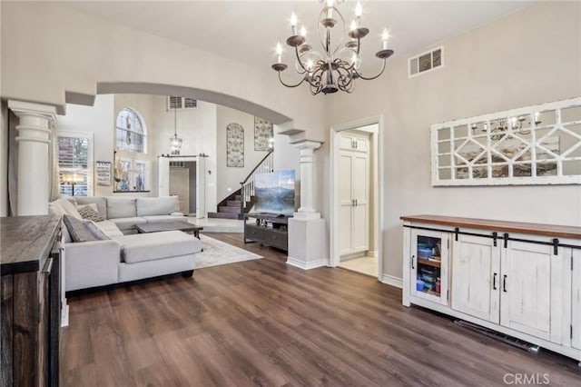 living room featuring arched walkways, visible vents, stairway, dark wood finished floors, and ornate columns