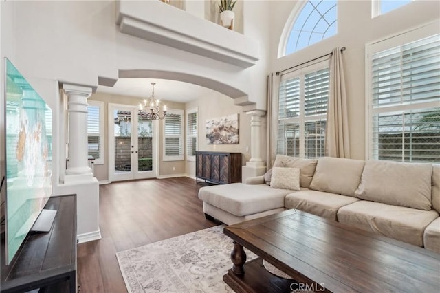 living room featuring dark hardwood / wood-style flooring, a notable chandelier, a high ceiling, and ornate columns