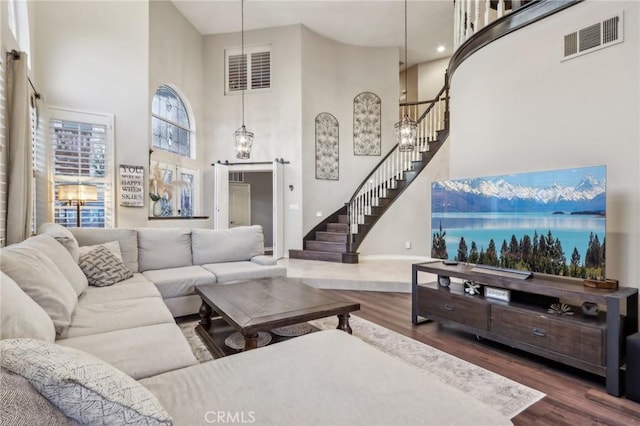 living room featuring dark wood-style flooring, a high ceiling, stairway, and visible vents