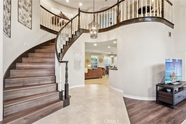 staircase featuring ceiling fan with notable chandelier, hardwood / wood-style flooring, and a towering ceiling