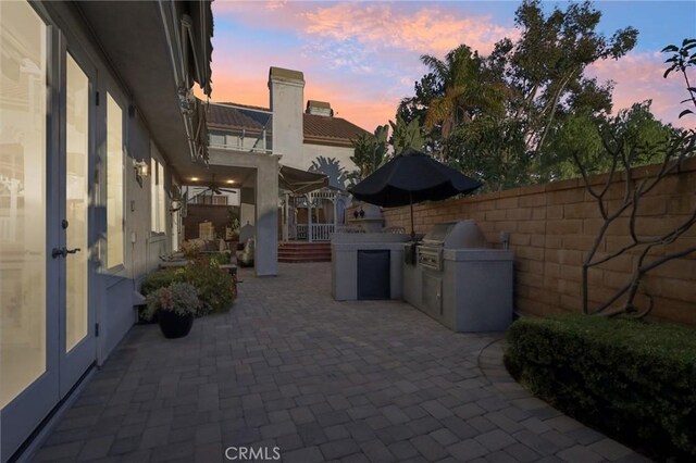 patio terrace at dusk with grilling area, an outdoor kitchen, and french doors