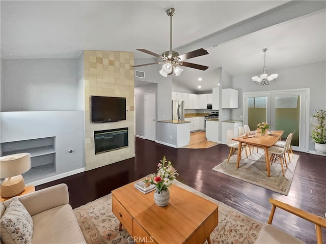 living room featuring ceiling fan with notable chandelier, vaulted ceiling, light hardwood / wood-style floors, and a tile fireplace