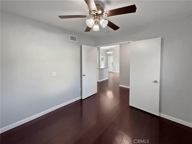 spare room featuring dark wood-type flooring and ceiling fan with notable chandelier