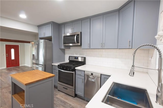 kitchen with stainless steel appliances, tasteful backsplash, light hardwood / wood-style floors, sink, and gray cabinetry