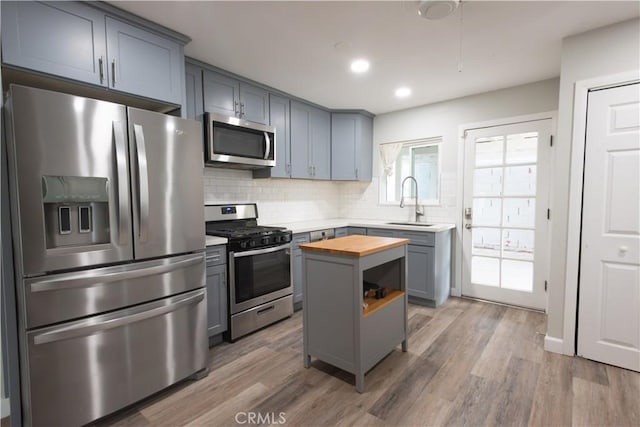 kitchen with hardwood / wood-style flooring, butcher block countertops, appliances with stainless steel finishes, sink, and a center island