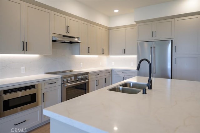 kitchen featuring high end appliances, decorative backsplash, light stone counters, and sink