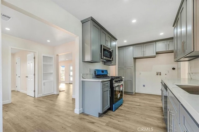 kitchen featuring appliances with stainless steel finishes, gray cabinetry, light stone counters, and light hardwood / wood-style floors