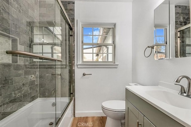 full bathroom featuring hardwood / wood-style flooring, shower / bath combination with glass door, vanity, and toilet