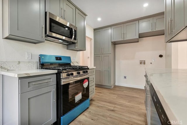 kitchen with gray cabinets, appliances with stainless steel finishes, light hardwood / wood-style flooring, and light stone countertops