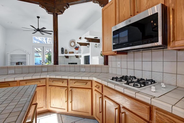 kitchen with backsplash, tile countertops, light tile patterned flooring, ceiling fan, and white gas cooktop