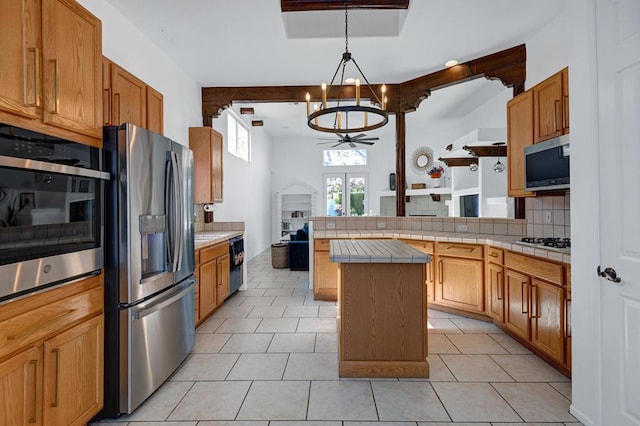 kitchen featuring tasteful backsplash, tile countertops, pendant lighting, a kitchen island, and appliances with stainless steel finishes