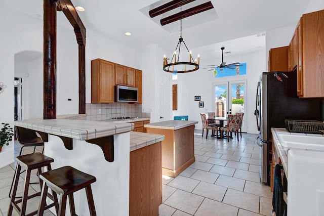 kitchen with tile countertops, a center island, kitchen peninsula, decorative backsplash, and stainless steel appliances