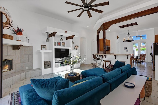 living room featuring ceiling fan with notable chandelier, light tile patterned floors, and a tiled fireplace