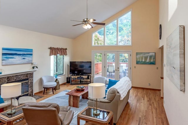 living room featuring high vaulted ceiling, ceiling fan, a premium fireplace, light wood-type flooring, and french doors