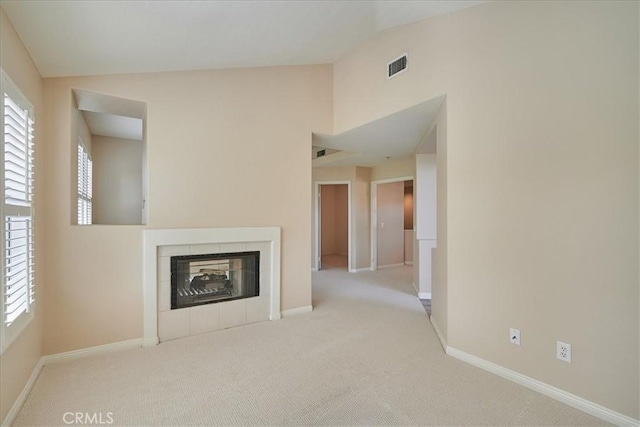 unfurnished living room featuring vaulted ceiling, light colored carpet, and a tiled fireplace