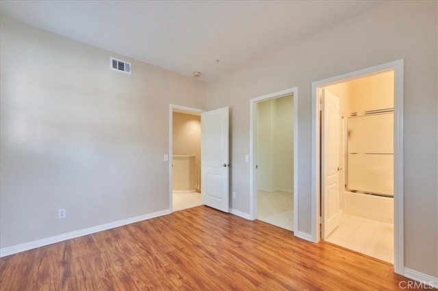 unfurnished bedroom featuring ensuite bathroom and light hardwood / wood-style flooring